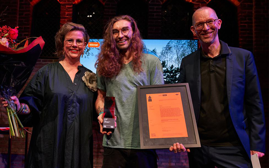 Lauréat des Dutch Design Awards tenant son trophée et un diplôme encadré à côté de deux autres personnes